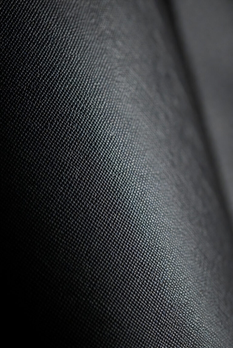 Close-up macro view of the iconic diagonal crosshatch texture of black Saffiano leather, showing the protective wax finish.