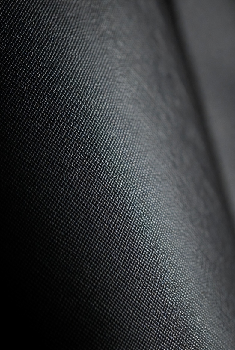 Close-up macro view of the iconic diagonal crosshatch texture of black Saffiano leather, showing the protective wax finish.